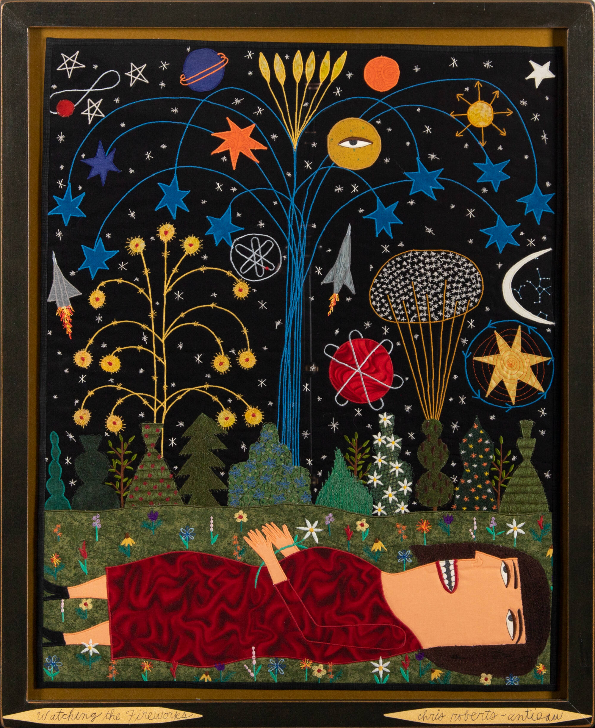 Textile artwork of a person laying on the ground, looking up at colroful shapes that represent fireworks.